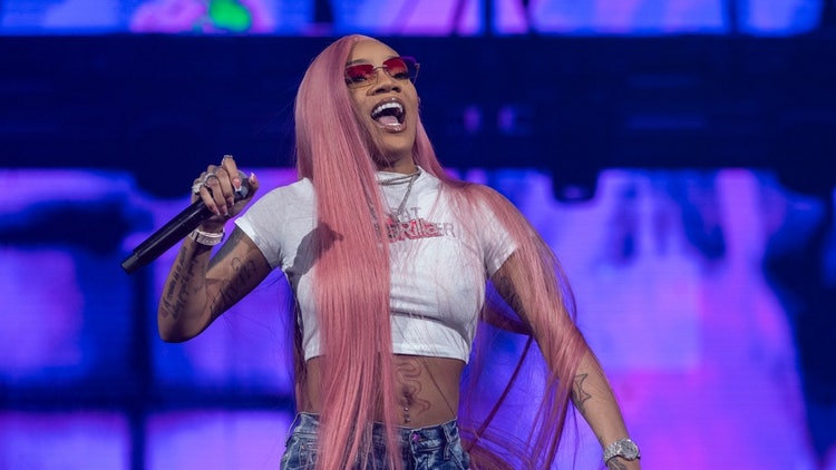 A person with long hair holding a microphone Description automatically generated