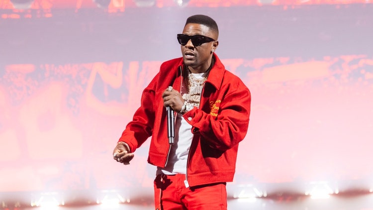 A person in red jacket and sunglasses holding a microphone Description automatically generated