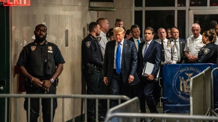 A person in a suit walking with police officers Description automatically generated