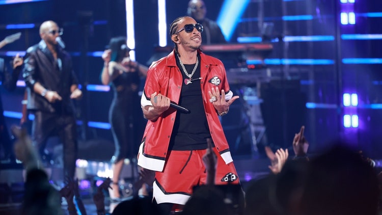 A person in red jacket and sunglasses holding a microphone Description automatically generated