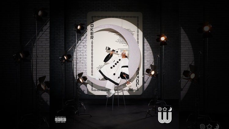 A person in a white suit sitting on a chair in front of a white circle with lights Description automatically generated