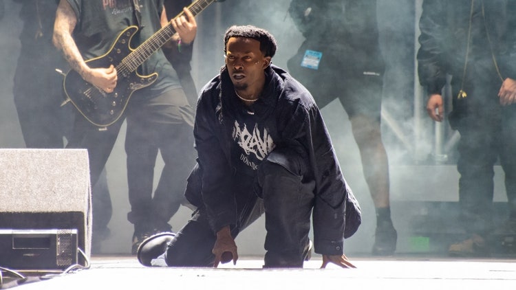 A person kneeling on the ground with a guitar and a person playing guitar Description automatically generated