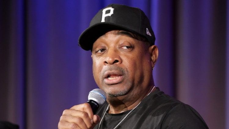A person wearing a baseball cap and holding a microphone Description automatically generated